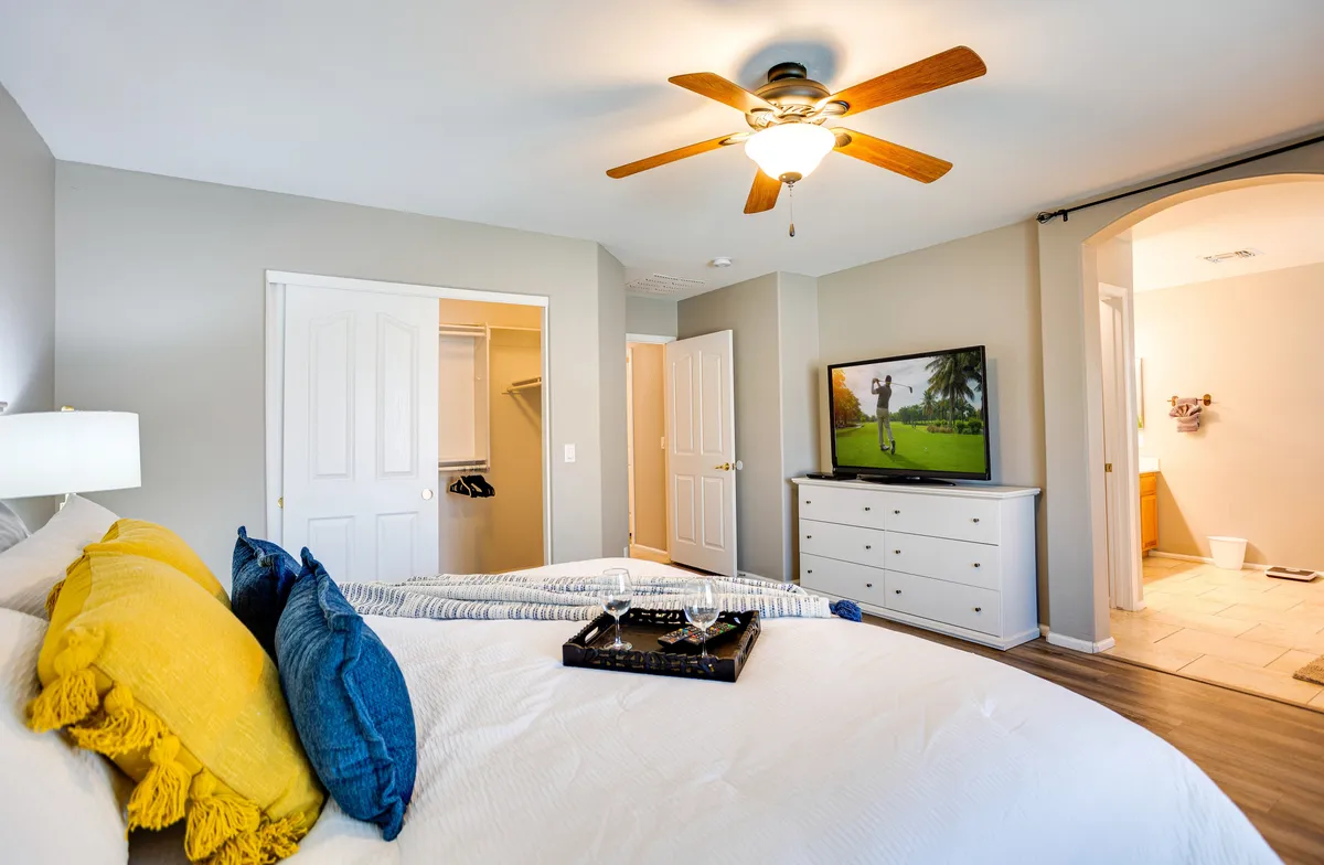 A neatly made bed with plush decorative pillows occupies the center of the room. A dresser holds a tray for added convenience, and a television, displaying a golf scene, is visible—subtly connecting to the Arizona setting. The room feels warm and comfortable, ideal for unwinding after a day of adventure.