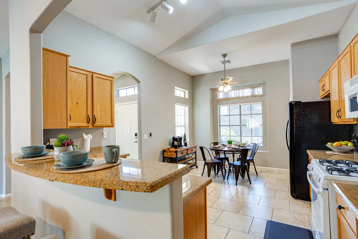 A bright and inviting kitchen and dining area featuring a spacious kitchen island, a family-sized dining table, large windows letting in natural light, and ample cabinetry. The scene showcases a space ideal for cooking, entertaining, and enjoying shared meals together.