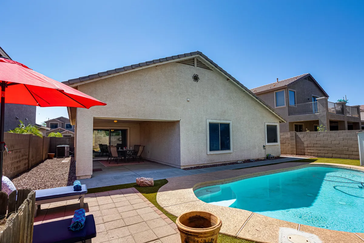 A closer look at the poolside reveals the patio area with comfortable outdoor seating, a red umbrella providing shade, and the swimming pool just a few steps away. The arrangement suggests a space perfect for outdoor dining, casual lounging, or sunbathing, with the promise of a relaxed, sun-filled Arizona afternoon.